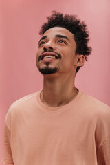 Obraz premium close-up of iridescent cute with beautifully shaved beard looking up on pink background. brown-eyed brunette with curly lush hair is wearing peach-colored T-shirt.