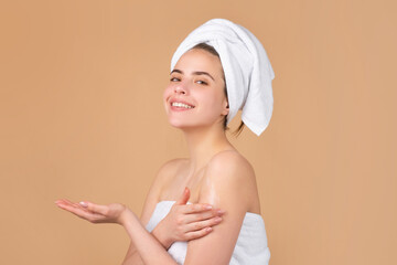 Beautiful smiling girl with clean fresh skin. Facial treatment. Cosmetology beauty and spa. Woman wrap towel on head put creme on healthy body skin.