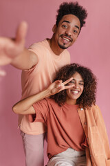 Obraz premium Young and impressive Brazilian couple playing with camera and having fun on pink background. Impressive high-quality shot of enthusiastic friends in casual clothes. Energy concept of human life