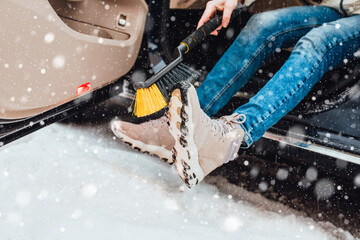 Woman in winter in heavy snow brushes shoes from snow before getting into the car - car care