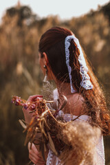 Portrait of a young brunette women in a white blouse and ribbon with a bouquet of dried flowers in the middle of the field. The beauty of autumn nature