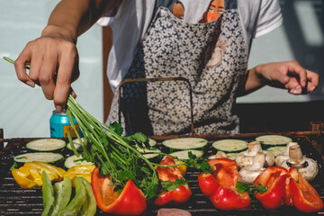 Young woman doing a vegan barbecue in a grill with various vegetables (mushrooms, red, green and yellow peppers and pumpkins) under the sunlight