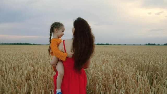 Little daughter on the rocks of the farmer's mother. The baby and mother are traveling in a wheat field. Happy family holiday. The child and the parent are playing in nature. Happy family on vacation.