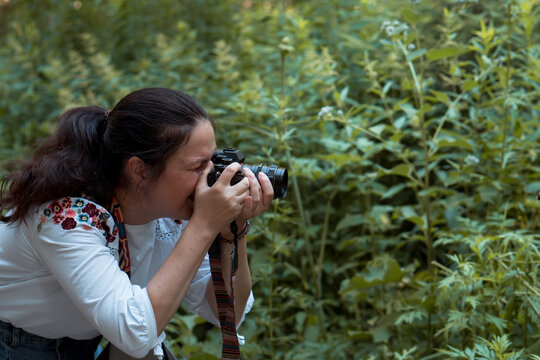 Caucasian woman taking photo pictures of plants on professional camera sony in summer forest or park 