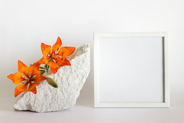 Mockup template with square white wooden frame, porous white stone and orange lilies on whiote background. © dariaren