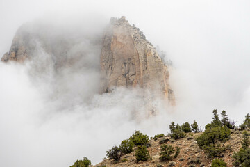 The mountains of Zion National Park in Utah with a heavy overcast and clouds dramatically passing in from of the peaks.  This unusual weather provides a dramatic feel and a sense of calm.