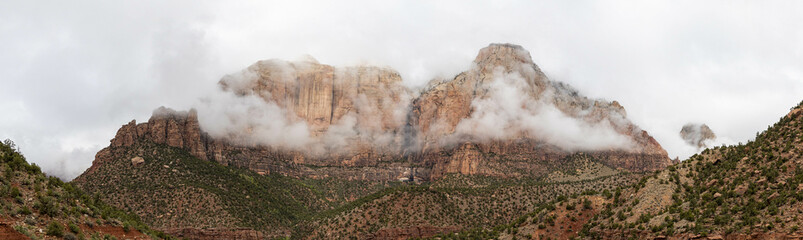 Panorama of the mountains of Zion National Park in Utah with a heavy overcast and clouds dramatically passing in from of the peaks.  This unusual weather provides a dramatic feel and a sense of calm.