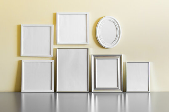 Set of many blank metallic silver and white wooden frames on yellow wall.