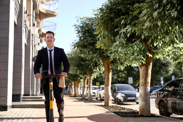 Excited stylish man rides an e-scooter on sidewalk near business center at daytime. Trendy urban transportation on modern electric scooter. Eco friendly mobility concept. Caucasian guy in formal suit