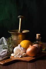 onion, garlic, lemon, rosemary and olive oil on a wooden board and green background.