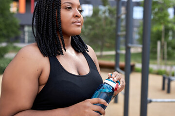 Relaxed african woman holding water bottle in hands going to drink after sport workout, conident...