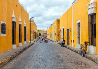 Mexican tricycle cab driver with passenger driving through the streets of the yellow city Izamal...