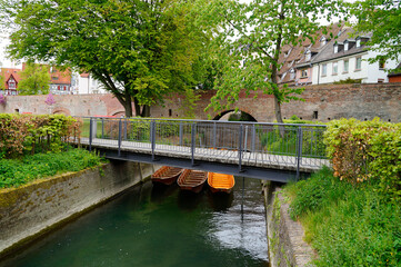 Fototapeta na wymiar a scenic view of a little bridge, wooden boats (Ulmer Schachteln) underneath it, green trees and the old town wall in the city of Ulm in Germany 