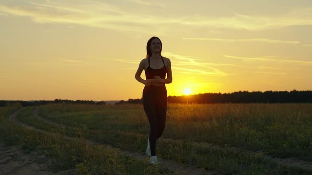 Training jogging. Free young woman runs in summer in park at dawn listens to music with headphones. Healthy jogging and outdoor exercise concept. Sports running for weight loss and health promotion