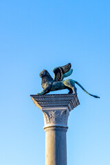 Bronze lion on the Piazza San Marco on blue sky background, Venice, Italy. Winged lion is a symbol of Venice. Ancient statue on a pillar close-up in Venice center