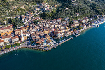Fototapeta na wymiar Brenzone sul Garda, Italy, September 2021, aerial view of Castelletto di Brenzone at Garda (Lake), showing the coastline with roads and the tranquil coastal villages with a small harbor (port)