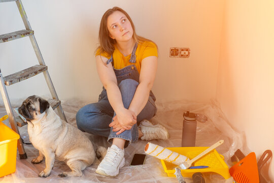 Independent young woman with pug dog planning renovation apartment sitting on floor with construction tool. diy repair owner hands with pet.