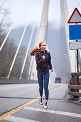 Focused runner outdoors running on the bridge, portrait of confident female athlete in sportive outfit jogging in the morning, sport activity in nature, foggy day. people lifestyle, sport concept