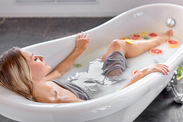 Side view on caucasian blonde female taking milk bath with lemons and oranges. Citrus spa. Body...