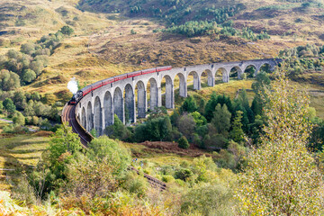 Glenfinnan-Eisenbahnviadukt in Schottland mit einer Dampfzugkreuzung. Das Viadukt wurde 1901 erbaut. Es ist mit 416 Yards (380 m) die längste Eisenbahnbrücke aus Beton in Schottland und überquert den Fluss Fi