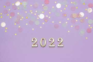 Numbers 2022 on lilac background are decorated with gold and pastel star confetti. New year concept. Banner, top view.