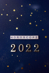 Word Horoscope and 2022 numbers. Wooden blocks with lettering on dark blue background decorated with stars confetti. Vertical flat lay.