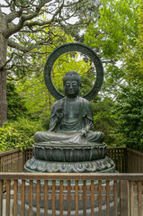 USA, California, San Francisco - May 19, 2008: Japanese Garden. Closeup of bronze sitting-on-lotus Protecting Buddha statue backed by green foliage.