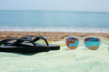 A closeup of sunglasses and slippers on a towel in the beach