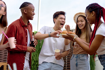 Excited young friends having fun at barbecue party outdoor in backyard. Young interracial people doing bbq dinner, eacting burgers, drinking lemonade. Youth lifestyle, food and friendship concept