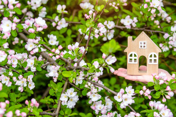 The girl holds the house symbol against the background of blossoming appletree
