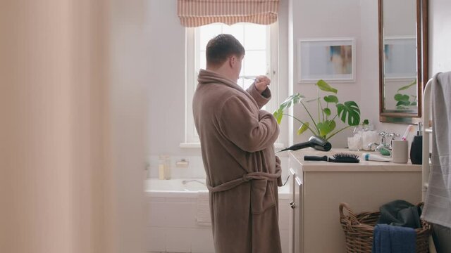funny teenage boy with down syndrome singing in bathroom using toothbrush having fun enjoying morning routine wearing bathrobe