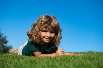 Portrait of a smiling child lying on green grass. Cute kid boy enjoying nature outdoors. Healthy carefree kid playing outside in summer park.