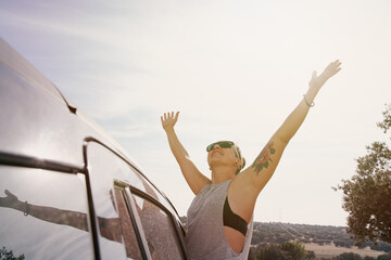 Woman looking out of car window with arms raised in happiness. Concept of travel, lifestyle and leisure activity.