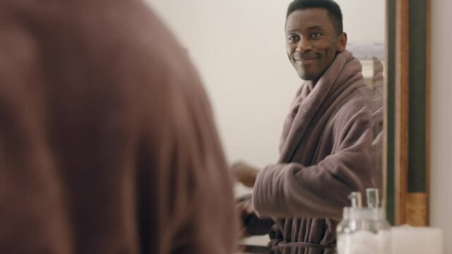 happy african american man dancing in bathroom looking in mirror having fun morning routine getting ready enjoying positive self image wearing bathrobe