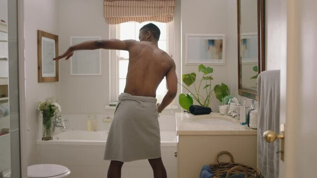 happy african american man dancing shirtless in bathroom looking in mirror having fun morning routine getting ready enjoying positive self image doing silly dance celebrating success