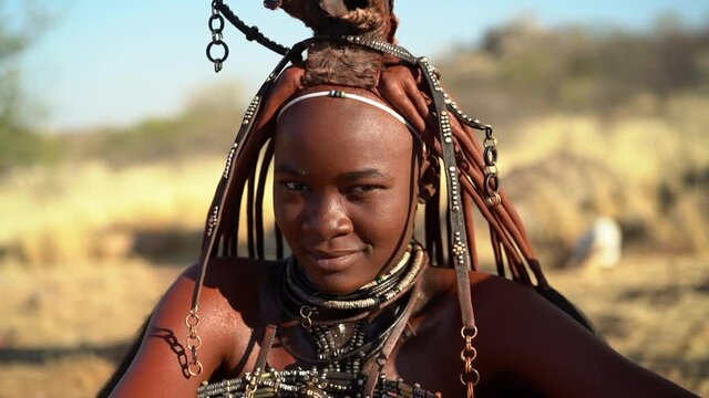 Beautiful Himba woman smiling, wearing traditional jewellery and headdress in her village near Kamanjab in northern Namibia, Africa, slow motion shot.