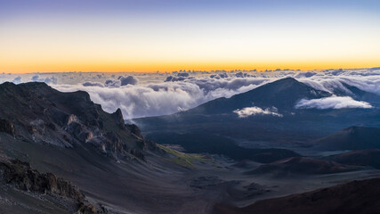 Clouds hang on jagged volcanic peaks during a dramatic morning sunrise in Haleakala National Park...