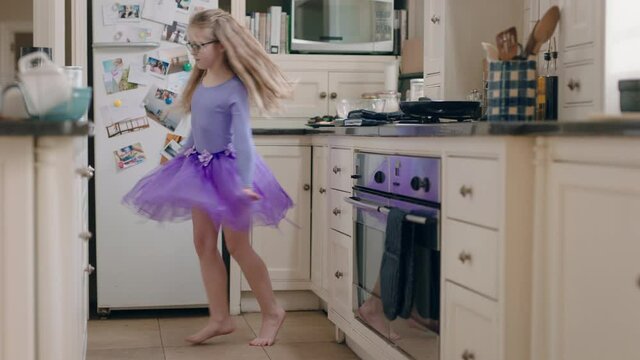 happy ballerina girl dancing in kitchen having fun practicing ballet dance moves wearing purple tutu at home