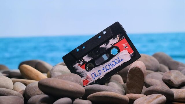 OLD SCHOOL sign on audio cassette label, which is laid on stone beach in midst of summer day by sea or ocean. concept of old warm memories long gone into oblivion.