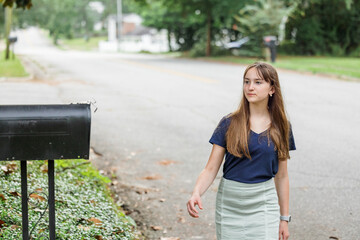 A teen brunette girl with long hair checking the mailbox for letters and packages.
