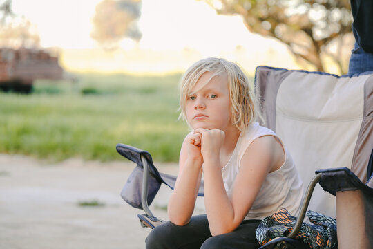 Boy Sitting On Fold Out Camp Chair Looking Bored