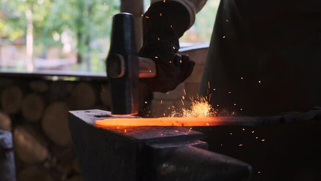 Blacksmith workshop in medieval on street. blacksmith knocks with large hammer and forms spear or sword, forges metal on anvil. Sparks fly in different directions.