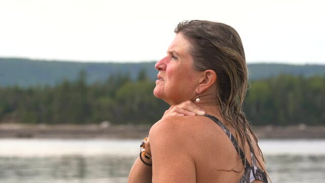 A mature woman experiencing nerve of muscle pain in her neck and shoulder after swimming at a beach.