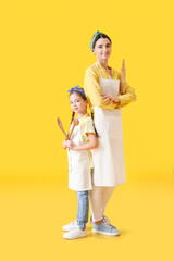 Young mother and daughter with kitchen utensils on color background