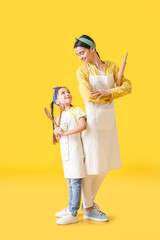 Young mother and daughter with kitchen utensils on color background