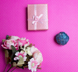 A flat lay photo of a bouquet of flowers, a gift in the form of a box and accessories on a pink background top view. High quality photo