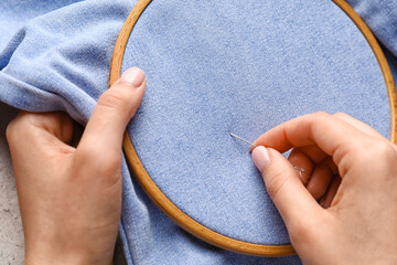 Woman sewing jeans on light background, closeup