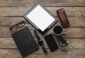 Different modern devices, eyeglasses and notebook on wooden background