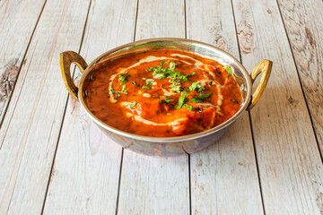 Chicken tikka masala mild curry with lots of fresh coriander on top in a traditional metal bowl
