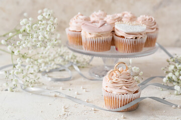 Tasty cupcake with wedding rings on light background